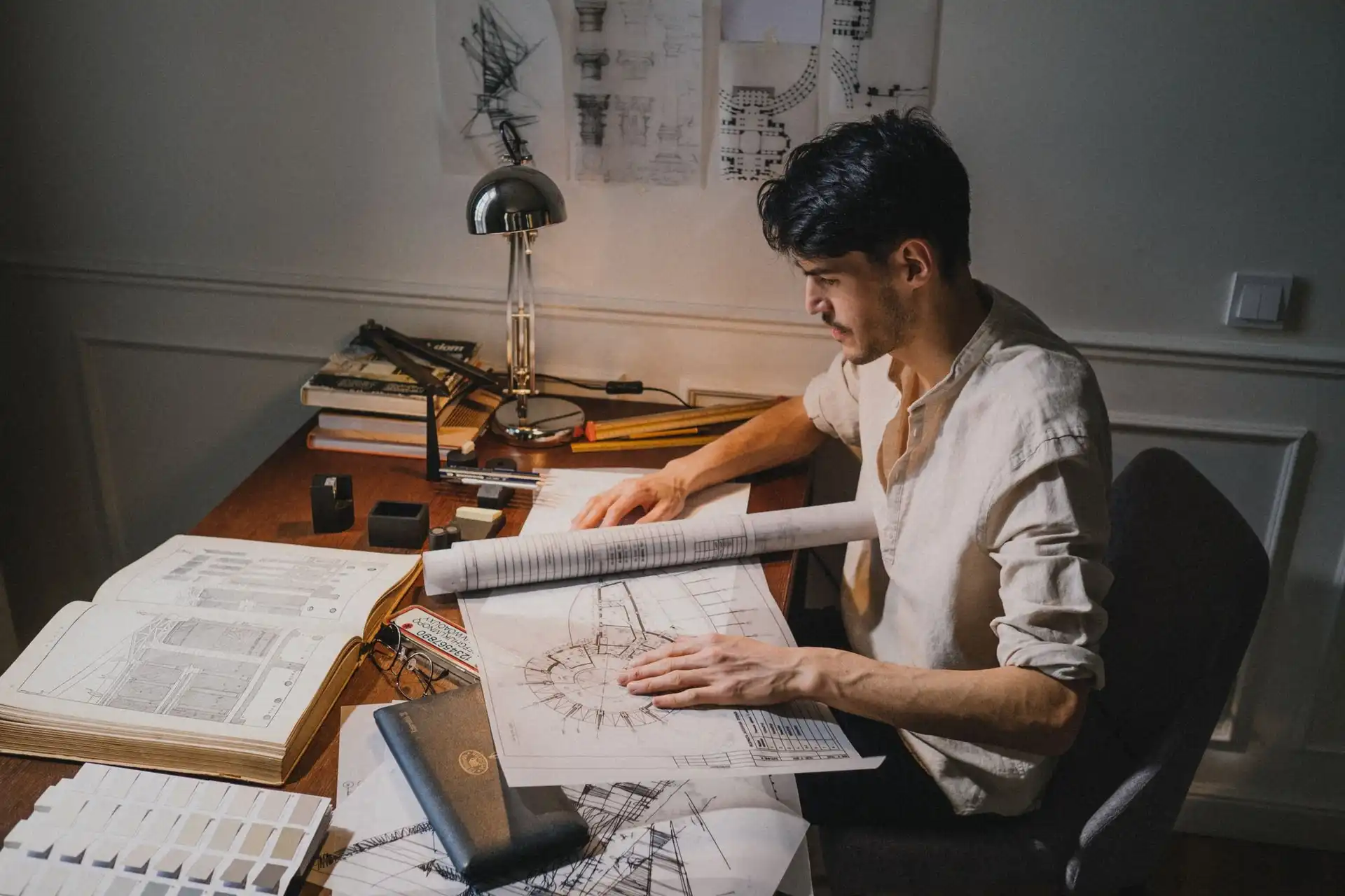 Un praticien seul à sa table de travail, penché sur des plans, sous la lampe